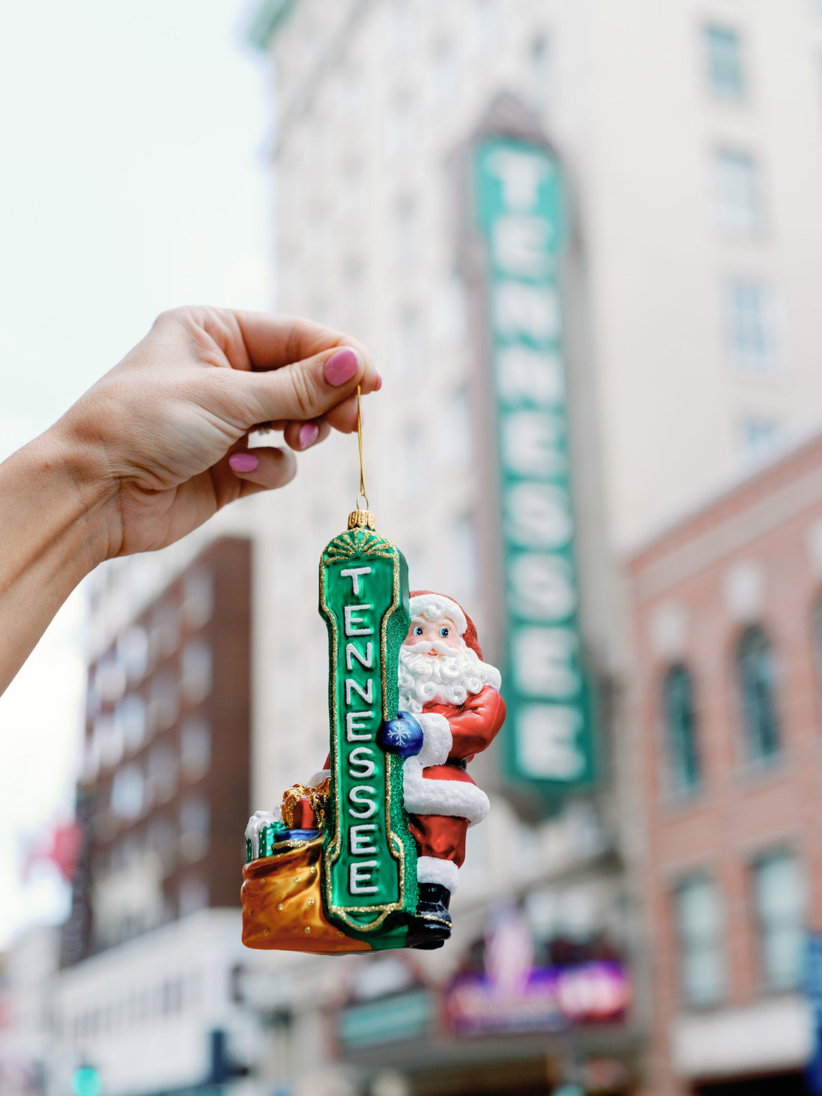 Tennessee Theatre Santa ornament held in front of the Tennessee Theatre sign